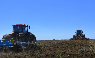 Red tractors plow the field. Rustic landscape. Agriculture. Farming