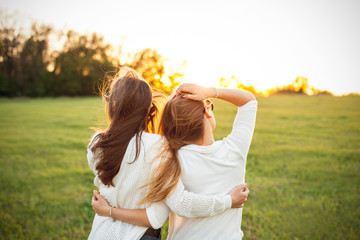 Two females are looking forward to the sunset on the green field.