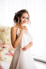 Fototapeta na wymiar Beautiful bride is holding her wedding dress in the boudoir room. look at the camera