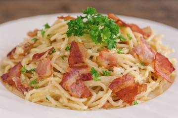Spaghetti carbonara with bacon and cheese on white plate sprinkle with chopped parsley on wood table in close up view. Italian traditional homemade food for lunch or dinner so creamy and delicious.