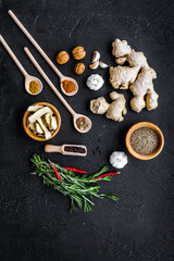 Condiments, seasoning and spices concept. Dry spices in wooden spoons near ginger, rosemary, chili pepper on black background top view copy space