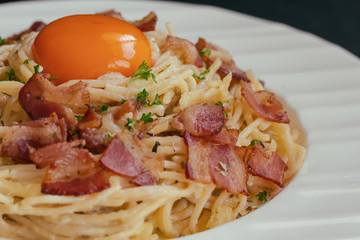Spaghetti carbonara with bacon, cheese and egg yolk on white plate sprinkle with chopped parsley in close up view. Italian traditional homemade food for lunch or dinner so creamy and delicious.