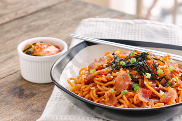 Korean hot and spicy instant noodle in blac bowl topped with bacon, sesame, seaweed and chopped...