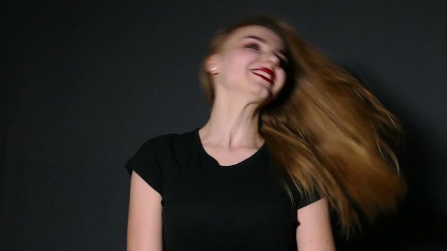 Young pleasant girl waves hair on dark background. Slow motion


