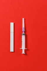 Two white cigarettes, empty syringe needle on red background. Health, choice, healthy lifestyle concept. Copy space for advertisement. With place for text. Stop drugs, narcotic, smoke.