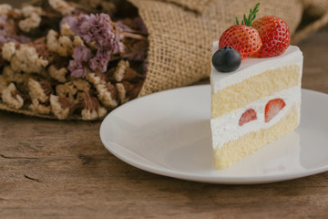 Strawberry shortcake on white plate put on wood table with copy space. Delicious and soft vanilla sponge cake with dairy whipped cream and fresh strawberries and blueberry. Homemade bakery concept.