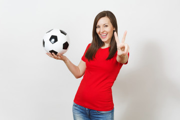 Attractive European young smiling woman, football fan or player in red uniform hold soccer ball, show victory sign isolated on white background. Sport, play football, cheer, healthy lifestyle concept.