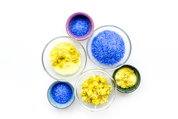 Colorful spa salt. Yellow spa salt with delicate spring flowers and violet lavender spa salt on white background top view copy space