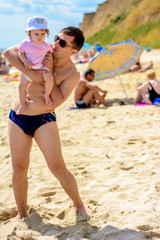 Young father in sunglasses on the beach with a little daughter