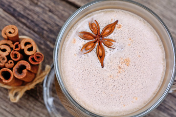 Glass with cappuccino and cinnamon sticks on table