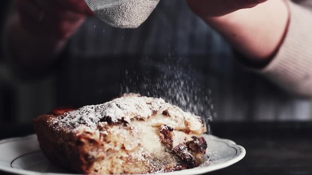 Slow motion shot hands of cook adding powdered sugar on the peice pie as a topping