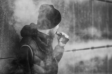 Vape man. Portrait of a handsome young white guy in black waistcoat and modern cap vaping an...