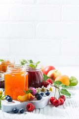 assortment of jams, fresh seasonal berries and fruits on white background, vertical