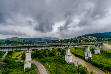 Fototapeta na wymiar Picturesque fairy tale landscape with a view at railway bridge and mountains covered with stormy rainy clouds. Fantasy colorful scenic route Hills and river. Tourist destination in Carpathians.