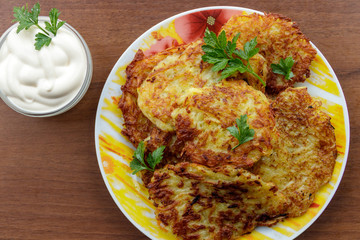 Homemade fried potato pancakes with sour cream on wooden table