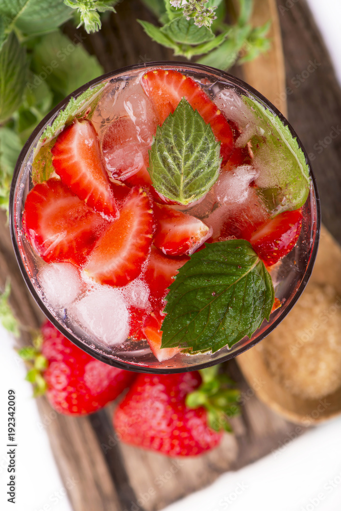 Sticker cocktail with fresh strawberries, mintand ice cubes over old white wooden table.