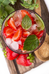 cocktail with fresh strawberries, mintand ice cubes over old white wooden table.