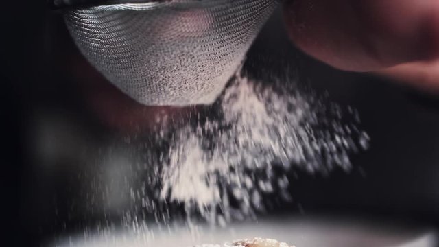 Slow motion shot hands of cook adding powdered sugar on the peice pie as a topping