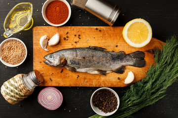 Fresh fish with herbs and spices on vintage cutting board on dark background, top view