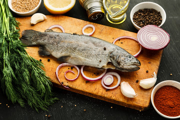 Fresh fish with herbs and spices on vintage cutting board on dark background