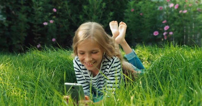 Child using cell phone and lying in grass. Dolly shot