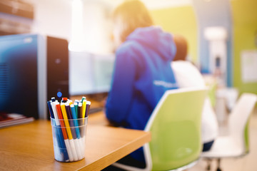 Workplace. People are sitting computer, working. Focus on glass with pencils