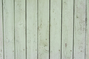 The old wooden fence. Texture of naturally aged light green fence with cracked paint. Close up 