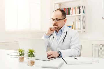 Fototapeta premium Serious doctor in glasses sitting at the desktop