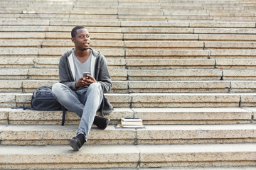 Happy african-american student using smartphone outdoors