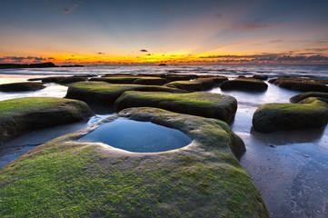 scenic view of sunset seascape with rocks covered by green moss on the ground.