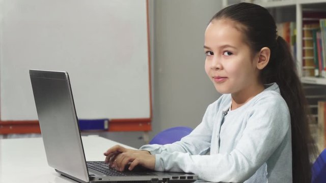 Happy beautiful Asian little girl smiling while using laptop