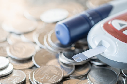 Close Up Of Glucose Meter With Lancet For Check Blood Sugar Level On Pile Of Coins Using As Medicine, Diabetes, Glycemia, Health Care And Money Concept.