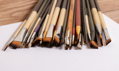 Many brushes for drawing lie on a clean white canvas on a wooden brown table