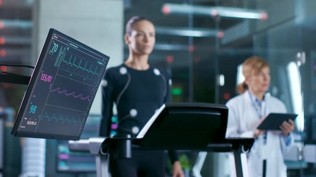 Monitor Showing EKG Reading of a Woman Athlete Walking on a Treadmill in the Background, Specialist Supervises Exercise, Controlling Physical Activity at Optimal Pace. Sport Science Theme.