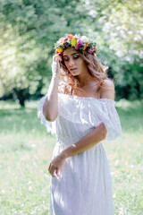 Beautiful bride in a white dress with floral wreath on hairs outdoor.