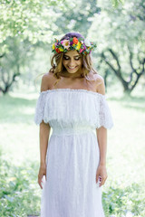 Beautiful bride in a white dress with floral wreath on hairs outdoor.