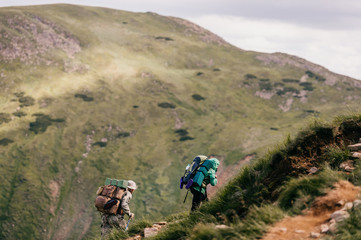 Obraz premium Travelers with backpacks and professional tourist equipment climbing carpathian mountains. Hard hiking. Conquest of high hills. Heavy luggage. Reaching top. Alpine walking. Vacation trip. Lifestyle.