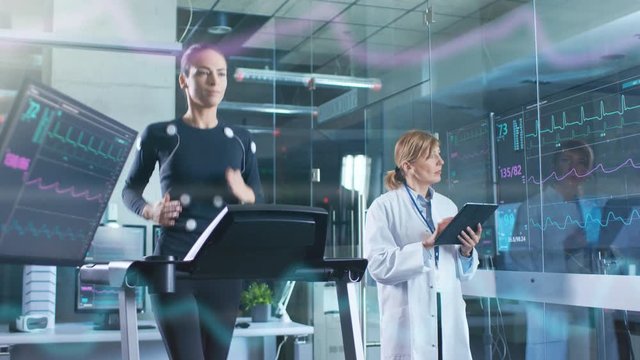 Woman Athlete Runs on a Treadmill  with Electrodes Attached to Her Body while Scientist Holding Tablet Computer Supervises whole Process.