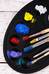 Palette with paints and tassels for drawing on a wooden table, top view