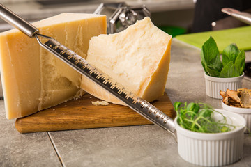 grated parmesan cheese and metal grater on wooden board with greenery
