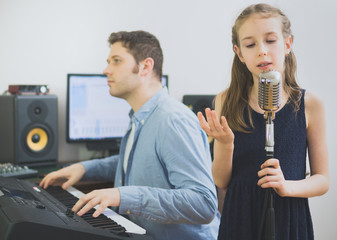 Man with little girl rehearsing song in music studio. Focused on girl.