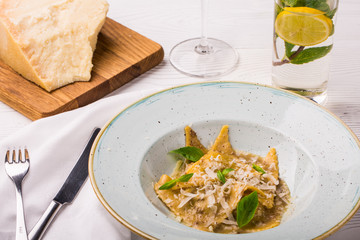Ravioli pasta with basil and parmesan cheese on plate. Parmesan with a grater on a cutting board