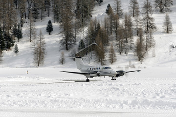 A front view of a private jet ready to take off in the snow covered landscape and mountains in hte alps switzerland in winter