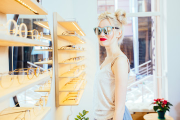 Young fashion woman with red lips and funny hairstyle trying sunglasses in optical store -...