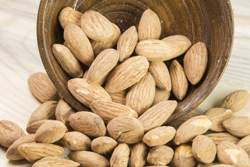 Almonds in brown bowl on textured wooden background, top view. Copy space on left side 