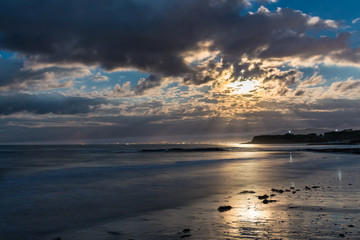 the full moon tries to peek through the clouds in the warm summer night from the beach of Foz, spain