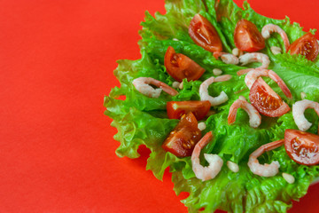 Salad of peeled shrimps and cherry tomatoes served on a leaf of fresh lettuce. Mediterranean Kitchen. Serving option. Close-up. Red background. With place for text. 