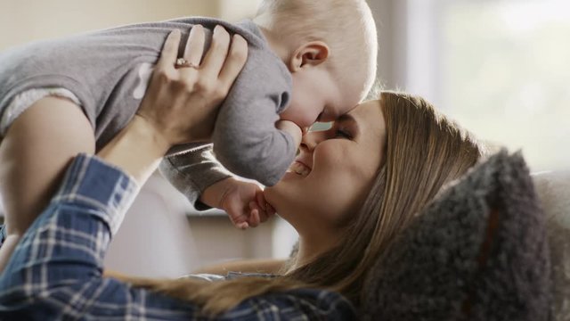 Mother laying on sofa kissing and rubbing noses with baby daughter / Alpine, Utah, United States