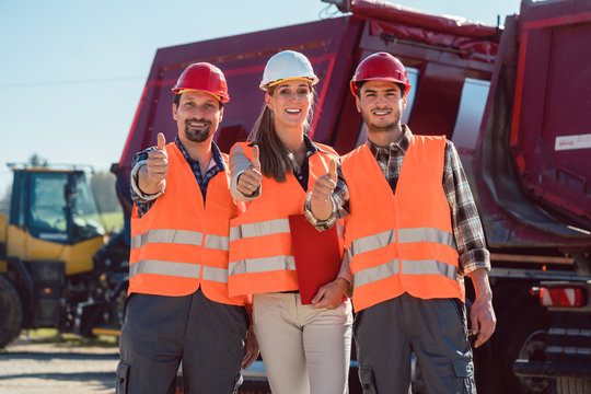 Colleagues in a freight forwarding company giving thumbs up in front of trucks