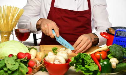 Cook burgundy uniform cuts vegetables. Male hands cut mushroom